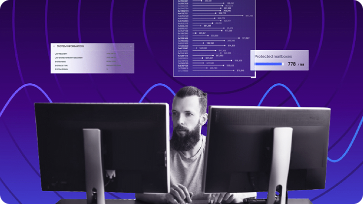 Person seated at a desk with dual monitors displaying system information and protected mailbox data, representing SIEM monitoring and security analytics